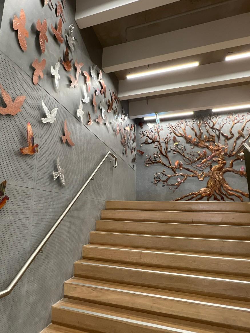 Aluminum birds along wall of stairs, above hand rail, leading to mother tree