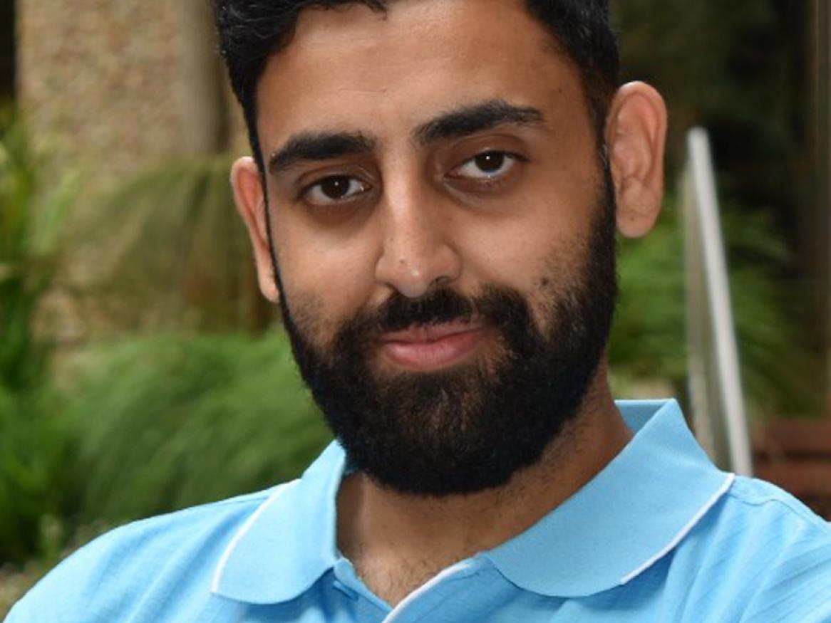 Photo of Aman Dhir, a man with black hair and a beard wearing a light blue tshirt with University of Adelaide logo