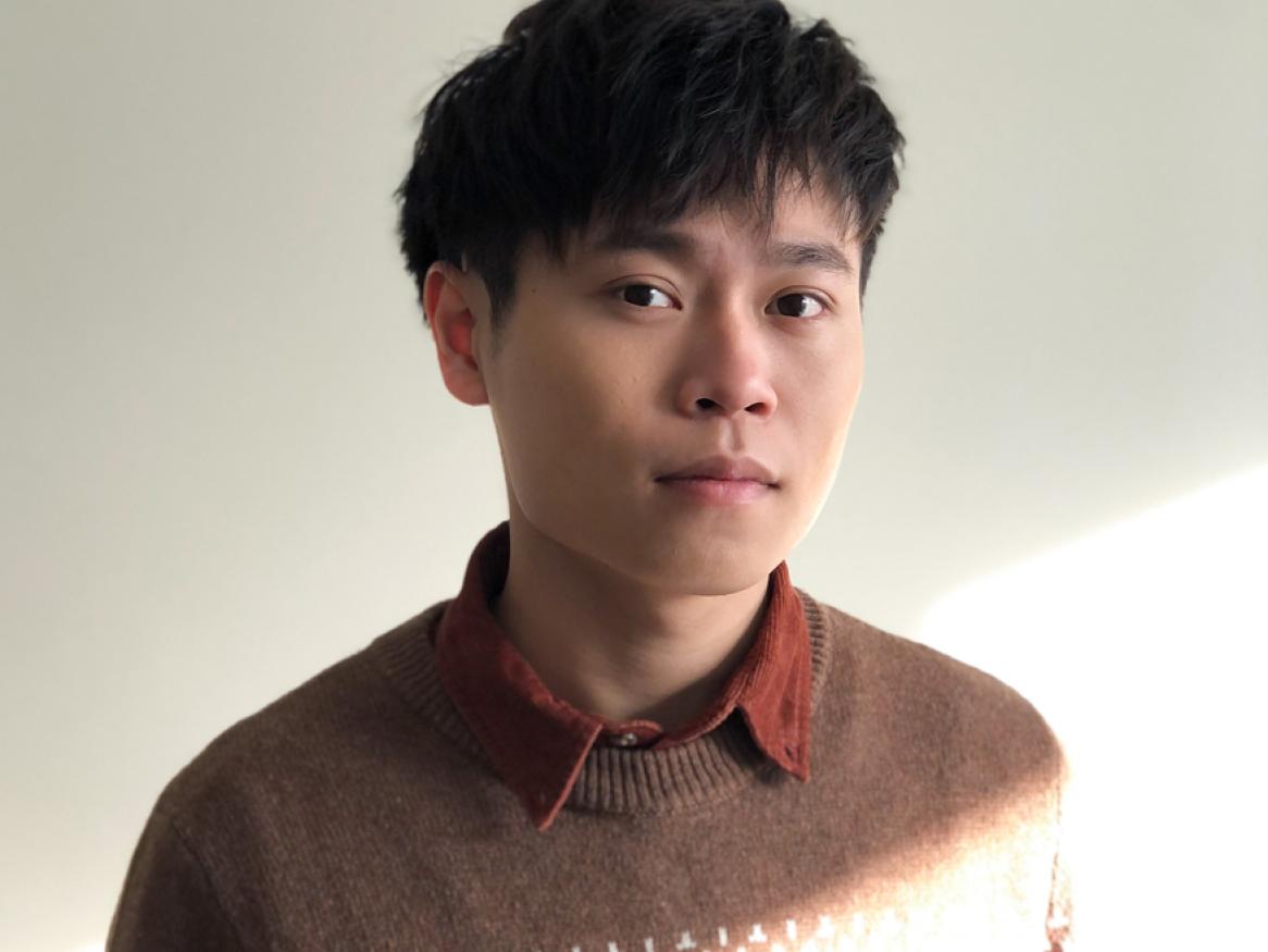 image of a man with black hair wearing a sweater and an orange shirt